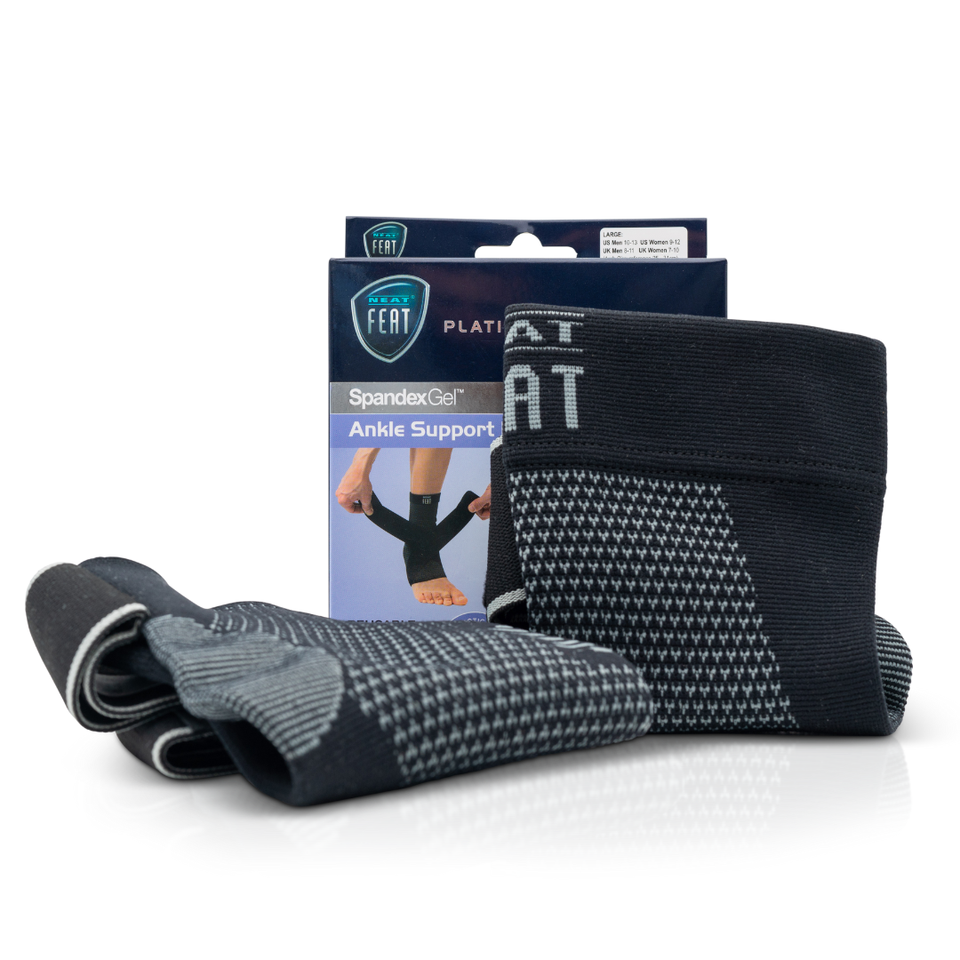 Platinum Series Spandex Gel Ankle Support Brace. The image shows the packaging box in the background, with two grey and black ankle braces displayed in the foreground. One brace is standing upright, while the other is lying down, showcasing the product's design and support features.
