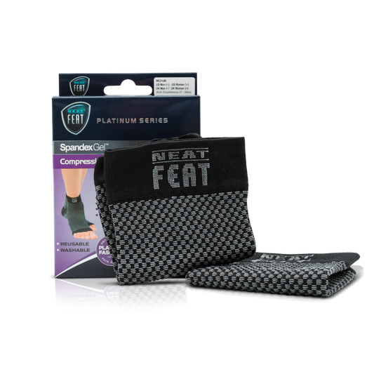 Platinum Series Spandex Gel Compression Arch Sock. The image shows the product box alongside the sock resting against it. The sock is black and grey, while the box is mostly dark blue and purple. The front of the box features an image of a foot demonstrating the fit of the sock, highlighting its arch support benefits.
