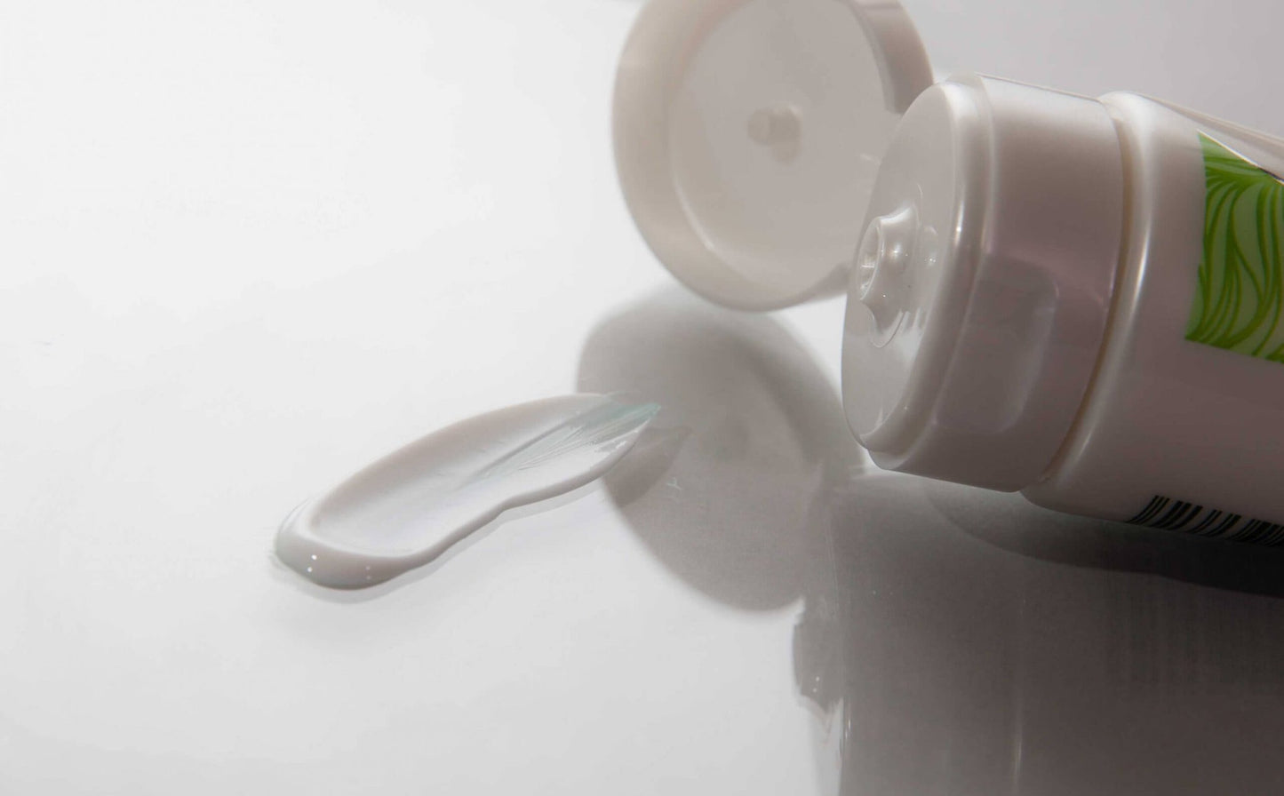 Close-up of the open cap of Neat Feat Natural Foot, Leg, Body & Hand Moisturiser, with some cream smeared on a white gloss table.