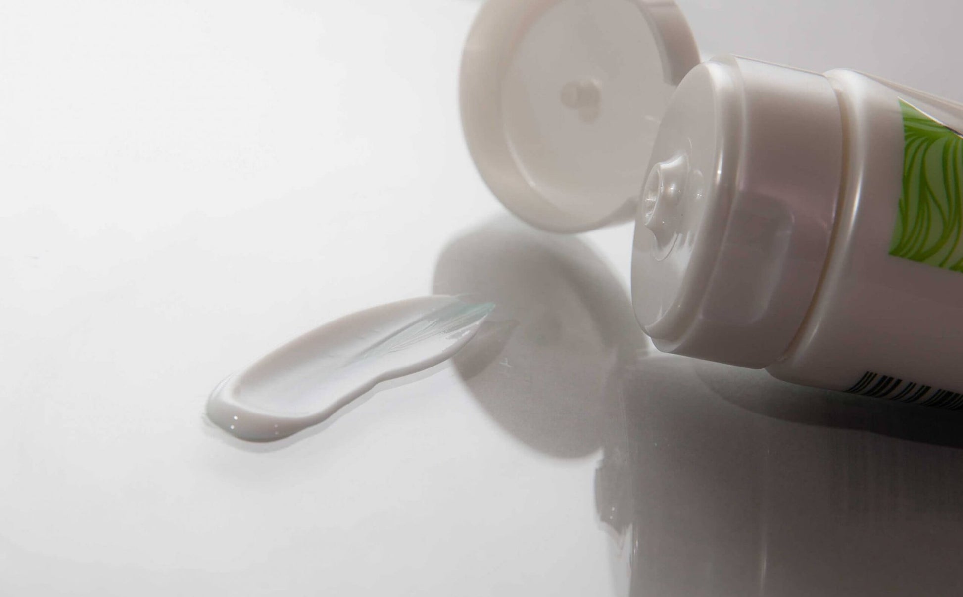 Close-up of the open cap of Neat Feat Natural Foot, Leg, Body & Hand Moisturiser, with some cream smeared on a white gloss table.